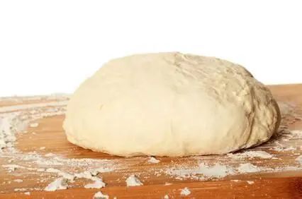 Ein runder Teigling ruht auf einem bemehlten Holzbrett, bereit zur Herstellung von Sauerteig in der Küche.