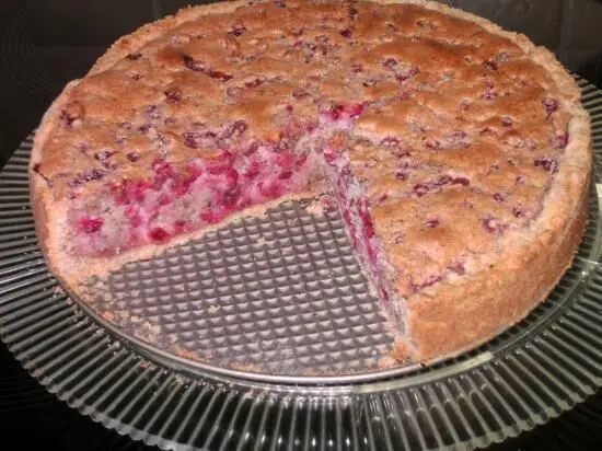 Ein Johannisbeerkuchen mit einem Stück herausgeschnitten, auf einem gläsernen Tortenteller, zeigt saftige rote Beeren.