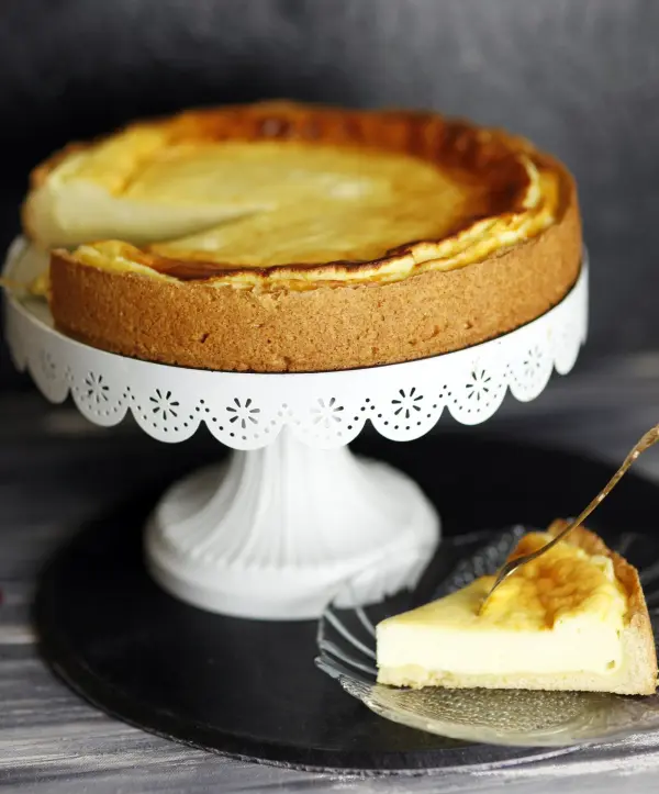 Ein Käsekuchen steht in einer eleganten Form auf einem Tisch, während ein Stück auf einem Teller geschnitten wird.