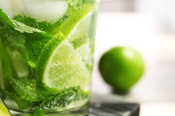 Ein Glas erfrischender Limetten-Minz Limonade mit Eiswürfeln und frischen Minzblättern steht auf einem Tisch, umgeben von einer Limette.