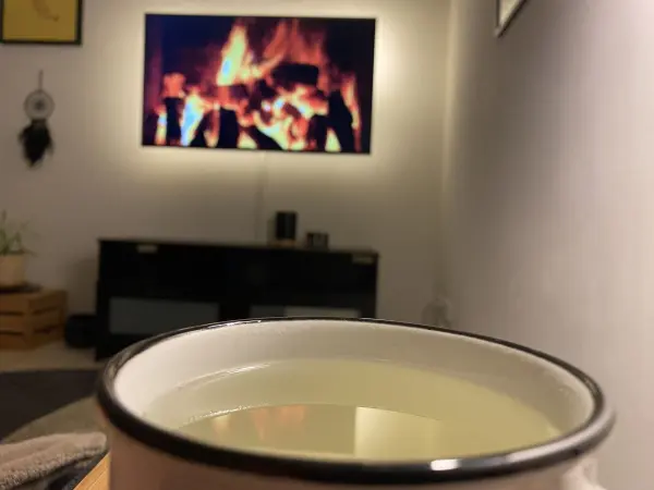 Eine Tasse Ingwer-Salbei-Honig-Getränk steht vor einem Fernseher mit einem Kaminfeuer im Hintergrund.
