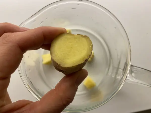Ein frischer Ingwer wird in einer Hand gehalten, während er über Wasserstücken in einem Glas schwebt.