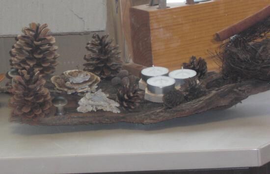 Eine dekorative Anordnung aus Naturmaterialien zeigt Zapfen und Kerzen auf einem Holzstück, ideal für weihnachtliche Deko.