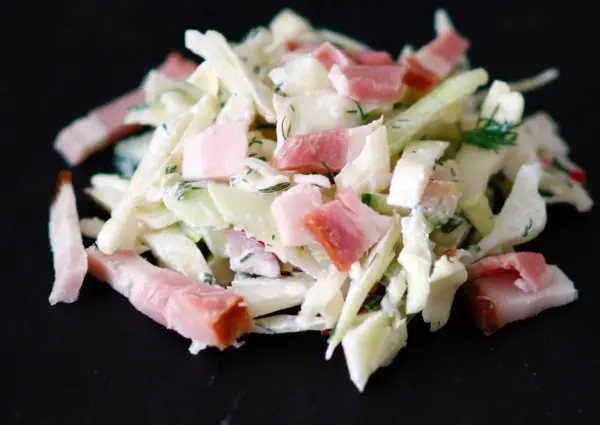 Warmer Krautsalat mit Speckwürfeln wird auf einem dunklen Teller angerichtet, frisch zubereitet und appetitlich angerichtet.
