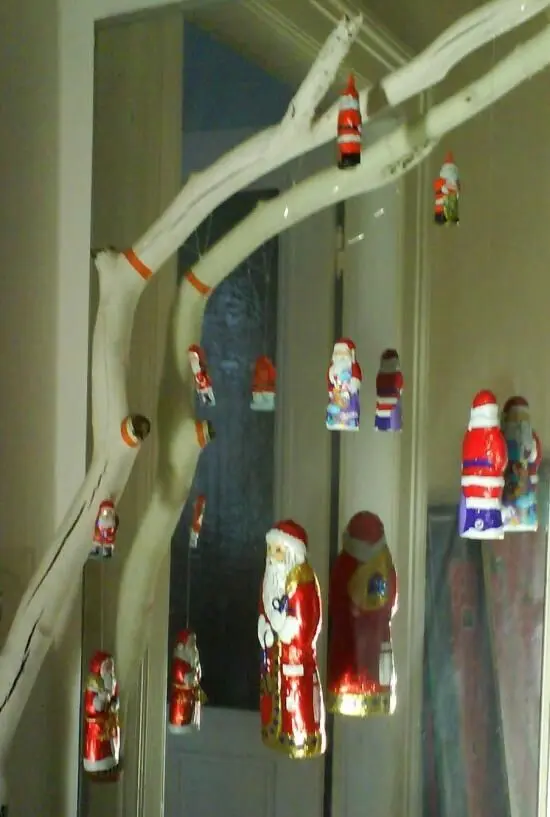Ein weißer Ast hängt dekorativ von der Decke, geschmückt mit bunten Schokoladen-Weihnachtsmännern in der Vorweihnachtszeit.