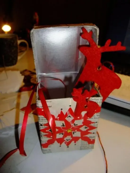 Eine dekorative Geschenkbox mit rotem Schneeflocken-Muster und einem roten Rentier an einem Innenrand, bereit für die Vorweihnachtszeit.