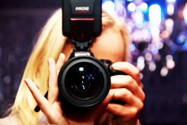 Eine Kamera wird von einer Person gehalten, die sich selbst fotografiert, umgeben von verschwommenen Lichtern.