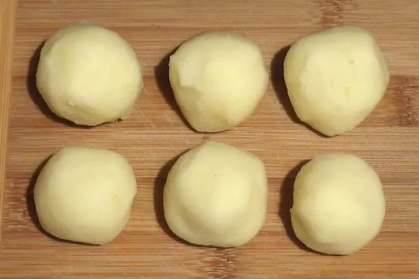 Sechs glatte, rohe Kartoffelklöße liegen auf einem Holzbrett und warten darauf, in einem Gericht verwendet zu werden.