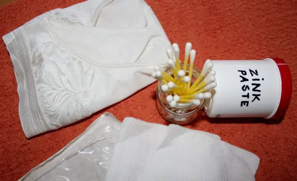 Weiße Unterwäsche und ein Glas mit Wattestäbchen liegen neben einer Zinkpaste auf einem orangefarbenen Tuch.