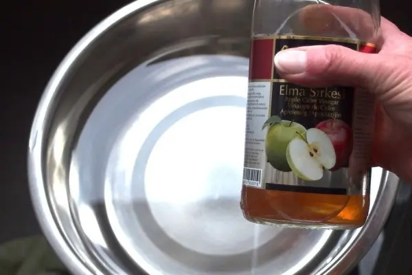 Ein Hand hält eine Flasche Apfelessig über eine glänzende Schüssel mit Wasser, bereit zur Mischung gegen Verstopfung bei Hunden.