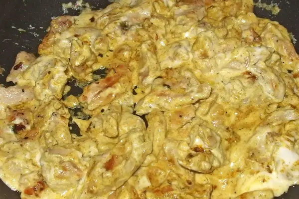 In einer Pfanne brät Curry-Geschnetzeltes mit zarten Fleischstücken und einer cremigen Sauce, umgeben von Gewürzen.