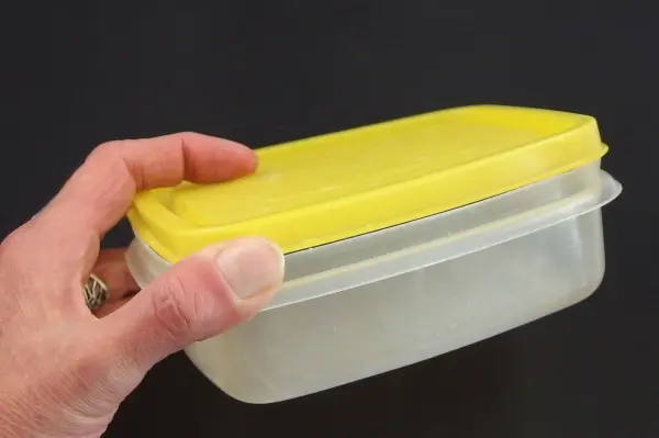 Ein Hand hält einen Kunststoffbehälter mit einem gelben Deckel, der leicht verzogen ist, um ihn wieder in Form zu bringen.