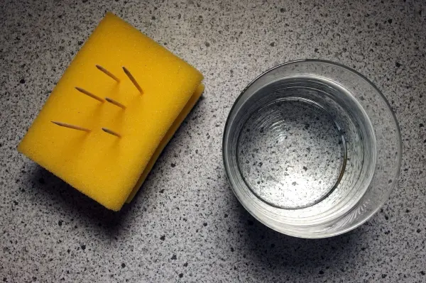 Ein gelber Schwamm liegt neben einem leeren Glas auf einer marmorierten Oberfläche, wobei der Schwamm für ausreichendes Trinken steht.