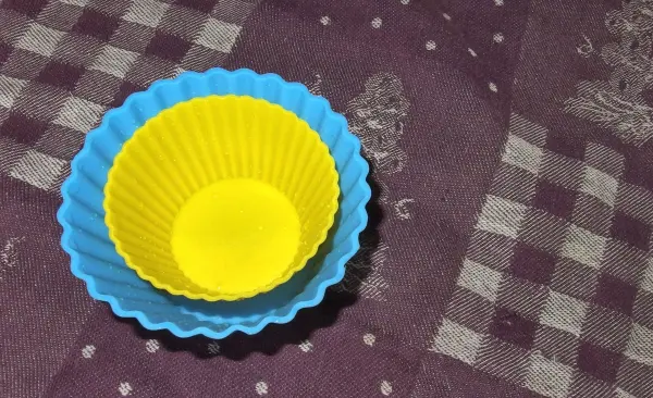 Zwei Silikonbackformen in Blau und Gelb stehen auf einem karierten Tisch, bereit zum Reinigen in Salzwasser.
