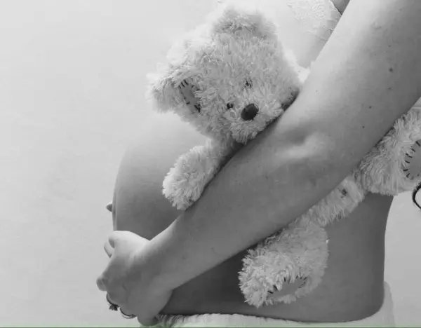 Eine schwangere Frau hält einen Plüschbären liebevoll an ihrem Bauch, symbolisiert die Geburtsvorbereitung in einem ruhigen Umfeld.