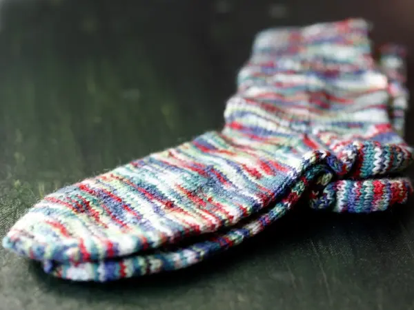 Bunte, gestrickte Socken liegen ordentlich auf einer dunklen Holzoberfläche, ideal für das Socken stricken.