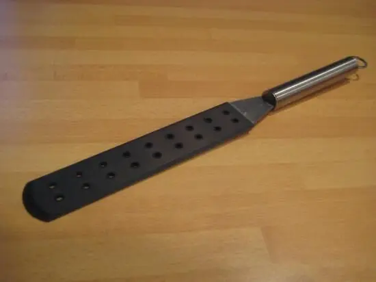 Eine Küchenutensilie mit einem langen, flachen Ende liegt auf einer Holzoberfläche, bereit zum Wenden von Crepes.
