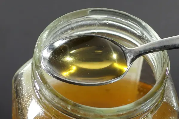 Ein Löffel mit flüssigem Honig steht in einem Glas, während der Honig in der Schale sichtbar bleibt.