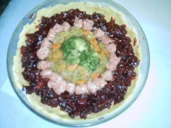 Eine Quiche Rondo aus gebackenem Teig, dekoriert mit verschiedenen bunten Belägen, entsteht in einer runden Form in einer hellen Küche.