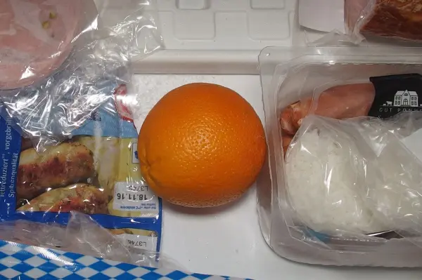 Eine Orange liegt auf einer Arbeitsfläche, umgeben von Verpackungen, bereit zum Schneiden für feine Orangenmarmelade.