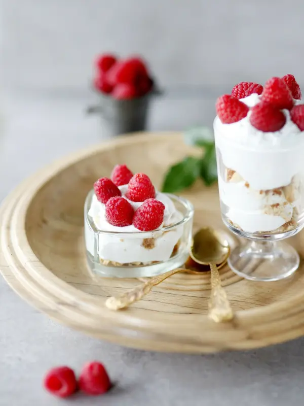 Zwei Desserts mit Himbeeren liegen auf einem Holzbrett, frisch mit Sahne und knusprigen Schichten, umgeben von Beeren.