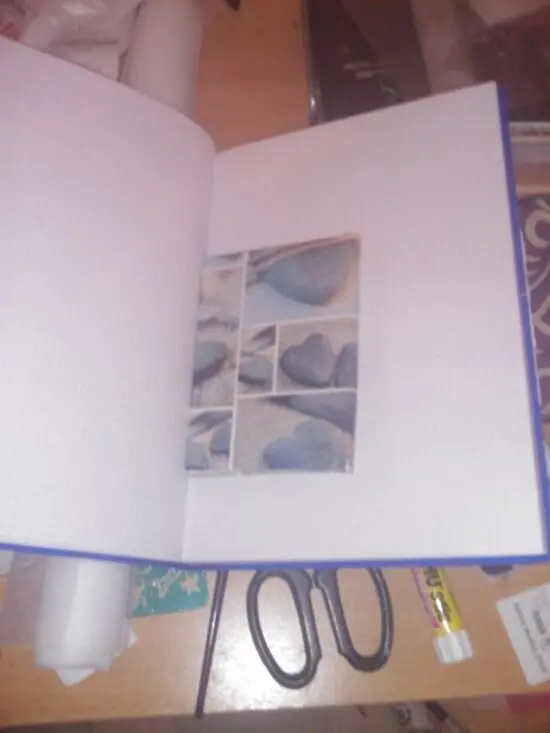 Ein offenes Notizbuch mit einem kleinen Fotobereich darin liegt auf einem Tisch, umgeben von Schere und Kleber.