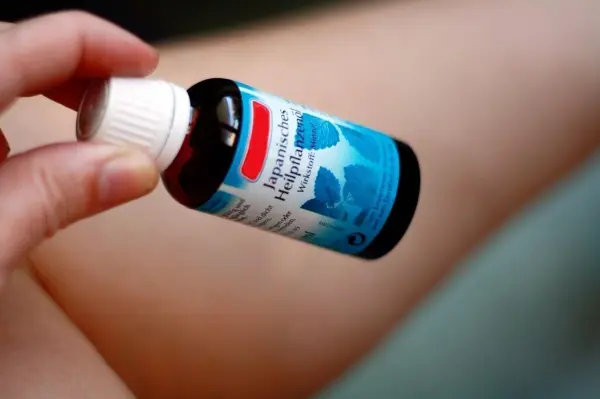 Ein Hand hält eine Flasche japanisches Heilpflanzenöl, während es auf den schmerzendem Kniegelenk aufgetragen wird.