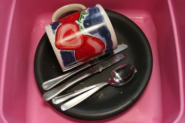 Ein bunten Becher und Besteck befinden sich auf einem tiefen Teller in einer Spüle, bereit zum Geschirr sammeln und spülen.