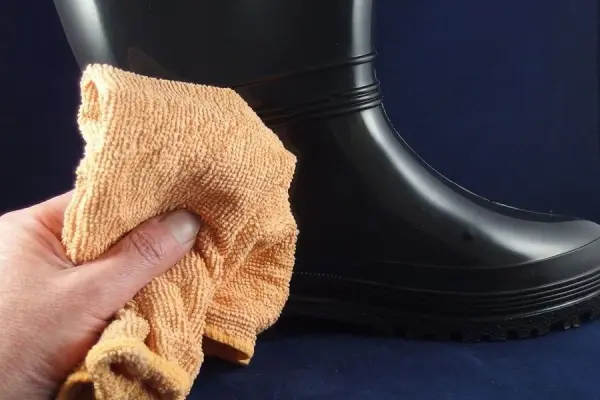 Ein schwarzer Gummistiefel wird mit einem orangefarbenen Tuch gereinigt, um die Haltbarkeit zu erhöhen.