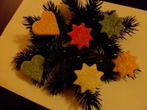 Bunte Wachsfiguren in Herz- und Sternform liegen auf einem Tannenzweig und schaffen eine festliche Weihnachtsstimmung.