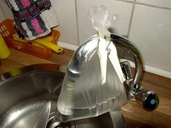 Ein Wasserhahn mit einem durchsichtigen Beutel gefüllt mit einer Reinigungslösung hängt über einer Spüle.