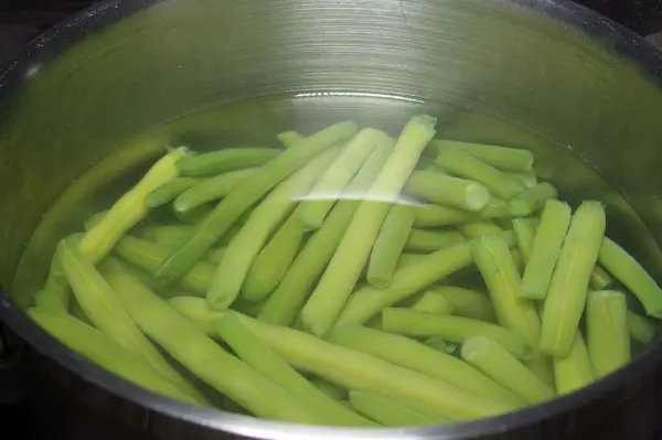Grüne Gemüsestängel schwimmen in einem Topf mit Wasser, bereit zum Kochen, um die Farbstabilität durch Kaiser Natron zu erhalten.
