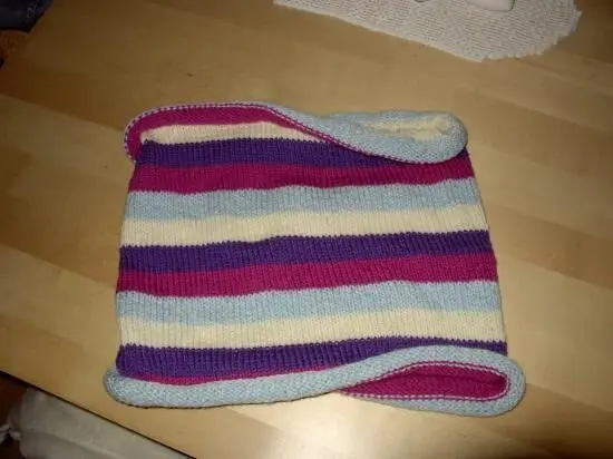 Ein gestricktes, bunt gestreiftes Stück liegt flach auf einem Holztisch.
