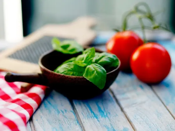 Ein Holzschälchen mit frischem Basilikum steht neben roten Tomaten auf einem Tisch, ideal für Ätherisches Basilikumöl.