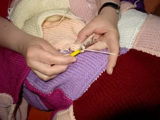 Gestrickte Hände nutzen eine Häkelnadel, um an einem bunten, gestickten Quilt weiterzuarbeiten.