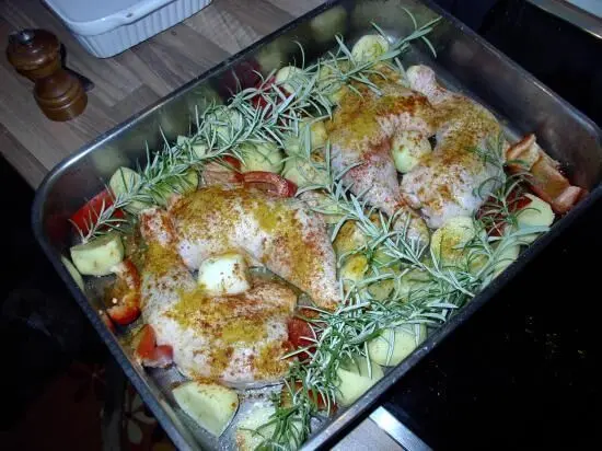 Zartes Hähnchen liegt mit Rosmarin-Kartoffeln und frischen Kräutern in einer Backform, bereit zum Braten.