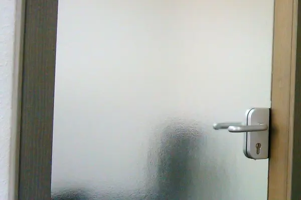 Eine Glastür mit Struktur befindet sich im Fokus, während sie gereinigt wird. Der Hintergrund bleibt unscharf.