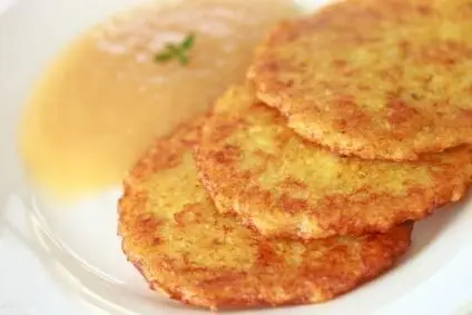Kartoffelpuffer liegen auf einem Teller, daneben Apfelmus. Sie sind goldbraun und fettarm, serviert auf weißem Geschirr.