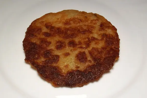 Ein fettarmer Kartoffelpuffer liegt auf einem weißen Teller und präsentiert seine goldbraune, knusprige Oberfläche.