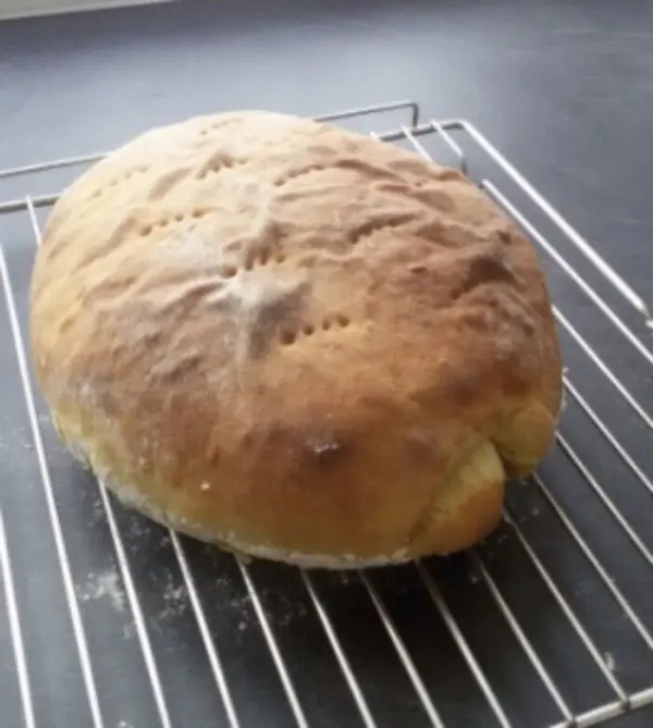 Ein goldenbraunes Siegerländer Kartoffelbrot liegt frisch gebacken auf einem Kuchengitter in einer modernen Küche.