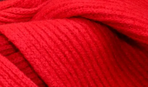 Ein rotes Wollstück liegt sanft gefaltet auf einem Tisch, bereit zum Glätten oder Aufrebbeln für ein Strickprojekt.