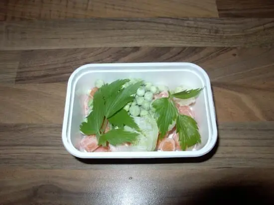 Eine Schüssel mit Tütensuppe wird verfeinert, umgeben von frischen Kräutern und Gemüse, auf einer Holzoberfläche.