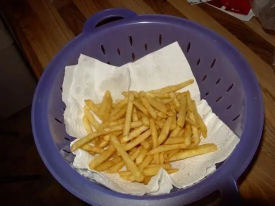 Pommes liegen in einem Sieb auf Küchenpapier, um nach dem Frittieren Fettreste abzutropfen.