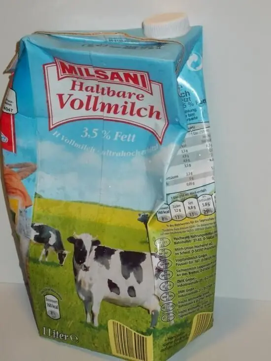 Eine Milchpackung steht auf einem Tisch, mit Bildern von Kühen und einer Wiese, die frische H-Milch zeigt.