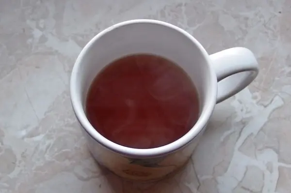 Eine Tasse Tee steht auf einem Tisch, dampfend und heiß, umgeben von einem schlichten, hellen Untergrund.