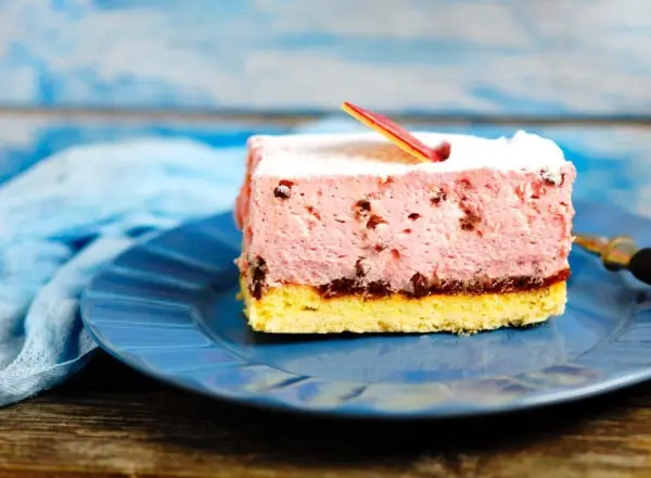Ein Stück Torte mit einer bunten Gelatinefüllung liegt auf einem blauen Teller, umgeben von einer rustikalen Holzoberfläche.