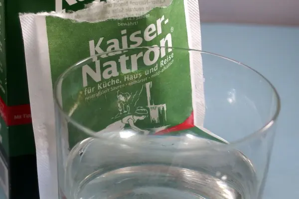 Ein Glas Wasser steht vor einer offenen Tüte mit Kaiser-Natron, bereit für die Anwendung bei empfindlichen Zahnhälsen.
