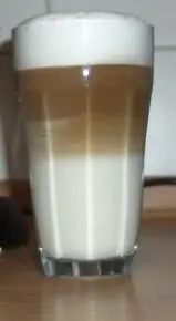 Ein zweifarbiger Latte Macchiato steht auf einem Holztisch. Die Schichten aus Milch und Espresso sind klar getrennt.