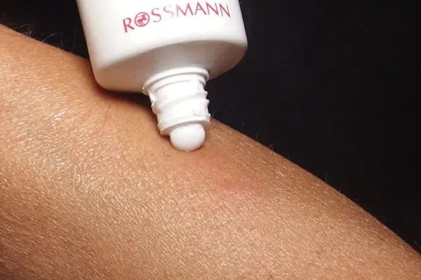 Eine Tube Zahnpasta lehnt über einem Arm, während sie eine kleine Menge auf einen Mückenstich aufträgt, um Linderung zu bieten.