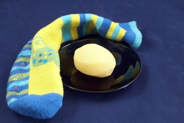 Eine heiße Kartoffel liegt auf einem schwarzen Teller, während ein bunter, gestrickter Socken daneben liegt.
